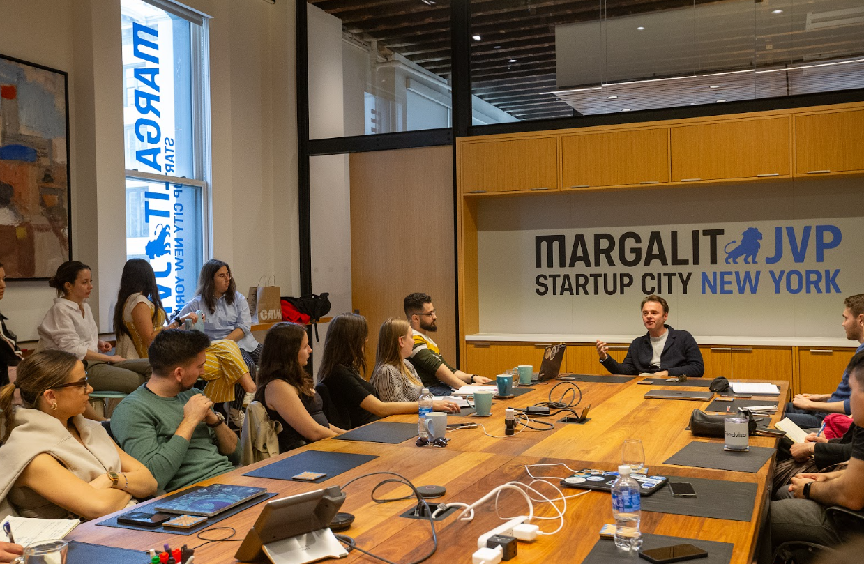 A group meets at "Margalit Startup City" for discussion, with laptops on the table. Keywords: Margalit Startup City, meeting, startup, tech.